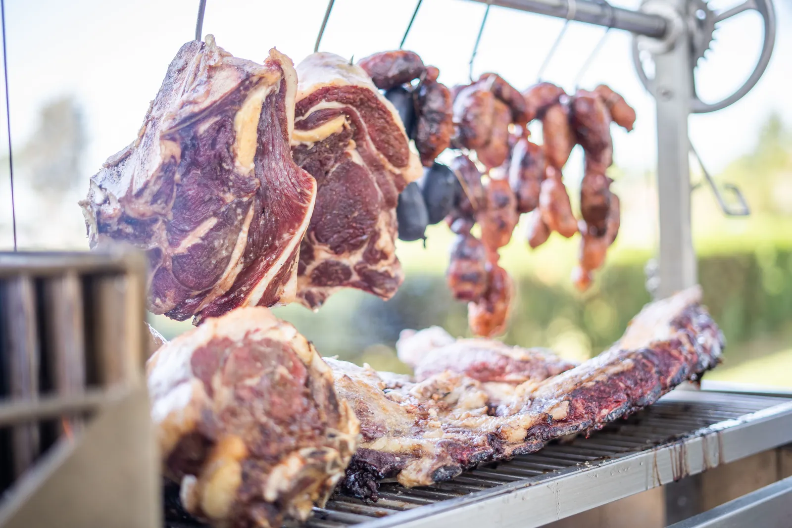 Beef ribs hanging from S-hooks over a Tagwood Santa Maria grill